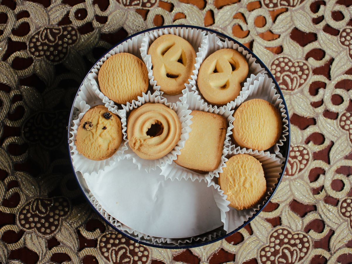 Butter cookies in paper cups inside a round tin, seen from above