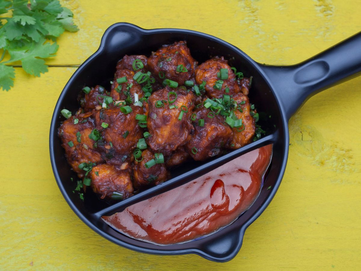 Cubes of chicken breast in a dark glaze with chopped spring onion, in a small black skillet, seen from above