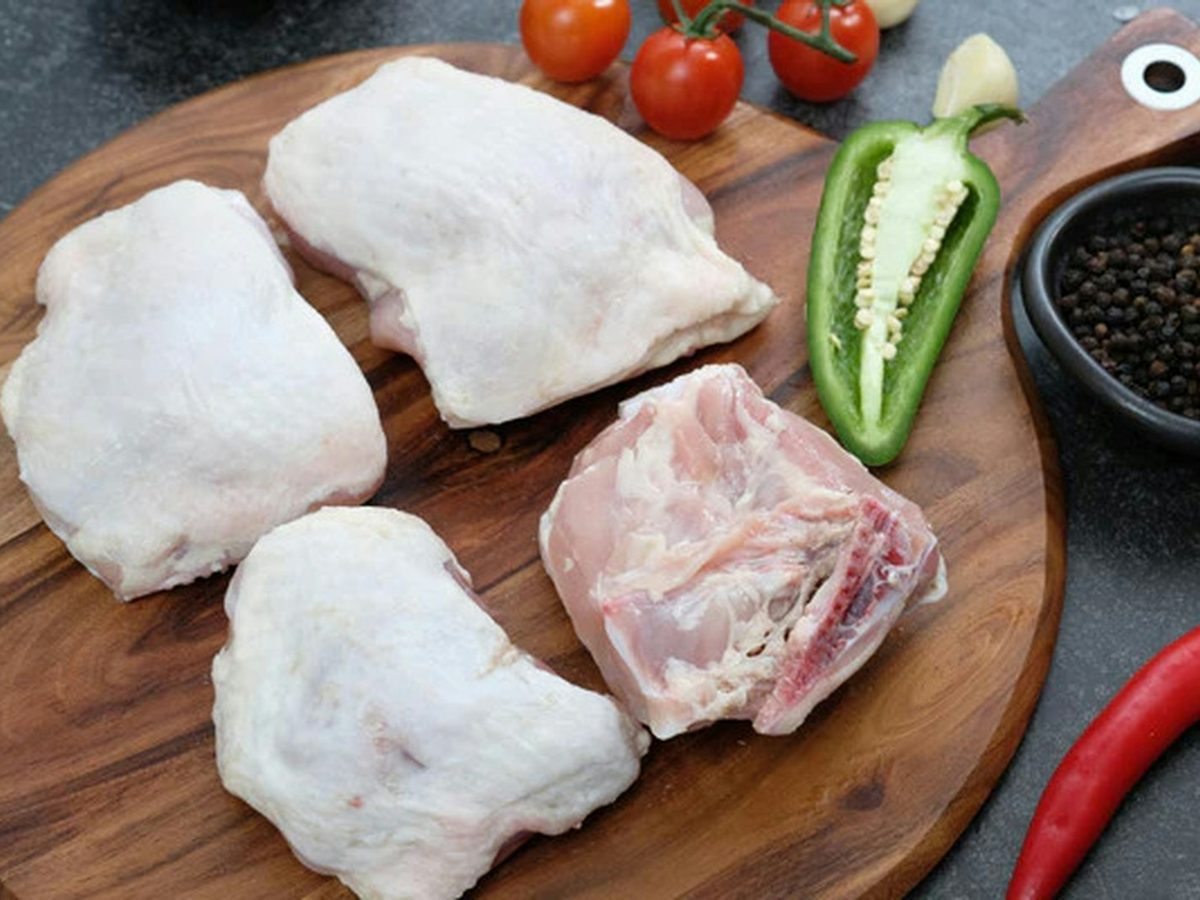 Raw chicken thighs on a board with chili, garlic and cherry tomatoes