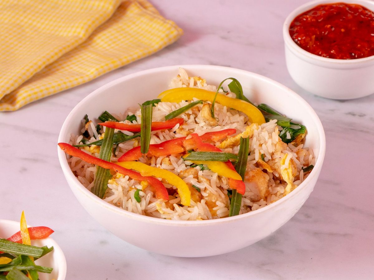 A bowl of chicken fried rice with red and yellow pepper strips