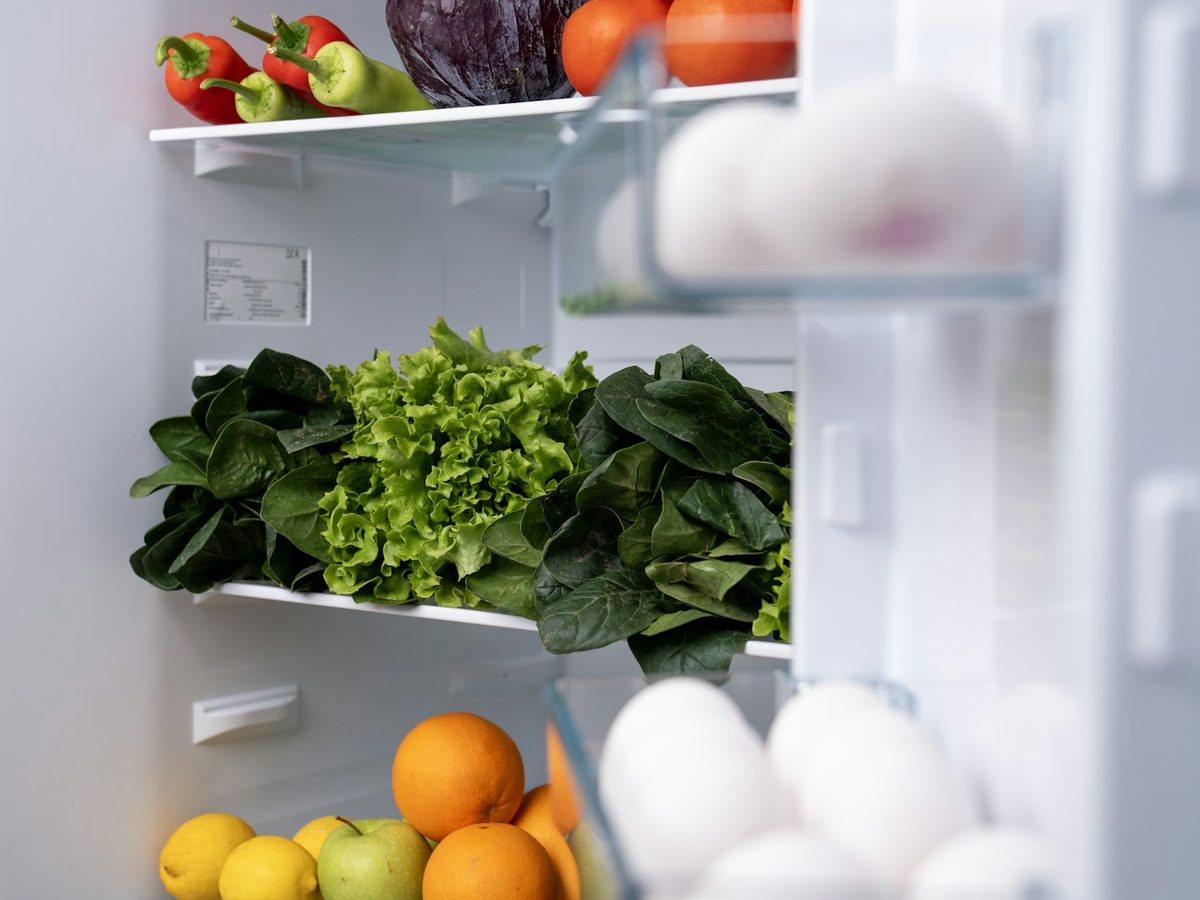 An open fridge shelf with vegetables and jars