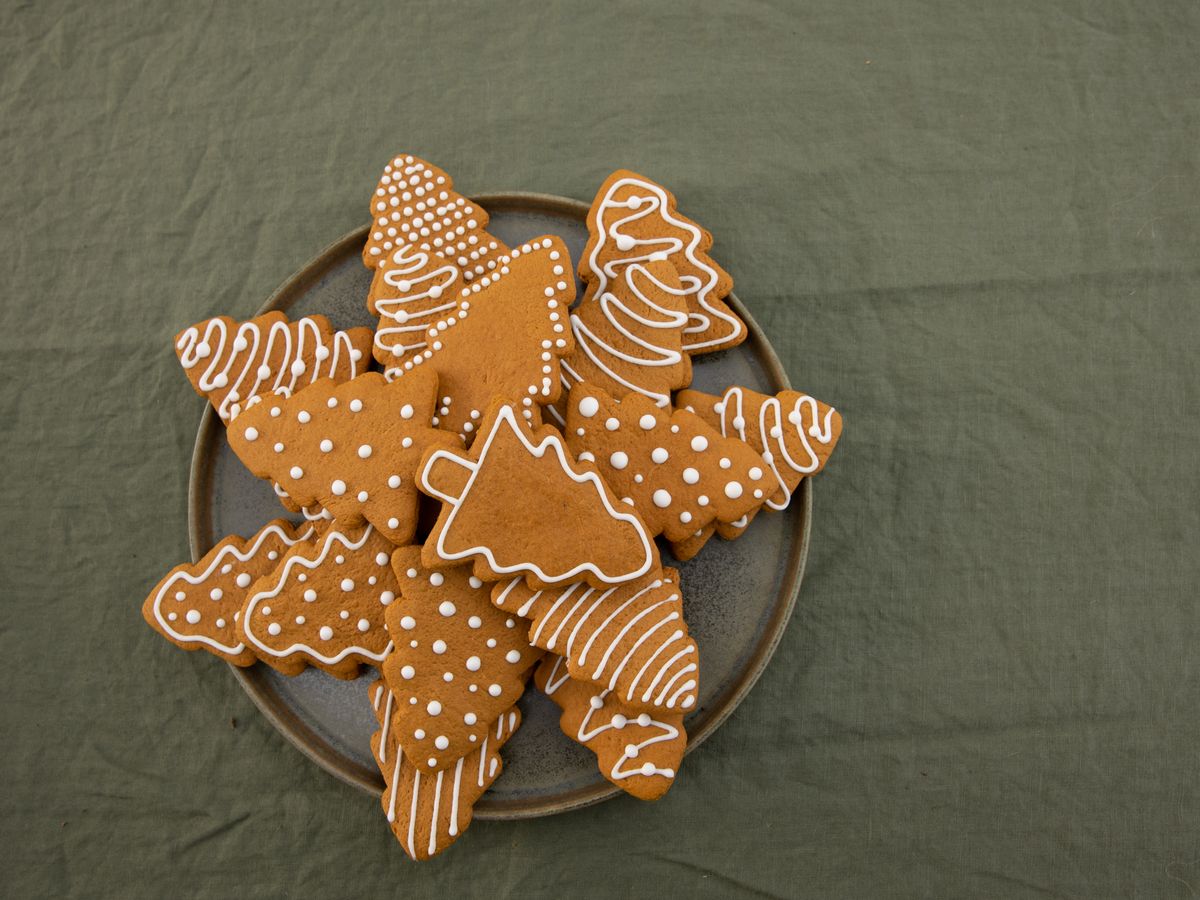 Tree-shaped gingerbread cookies piped with white icing on a grey plate, green linen under it