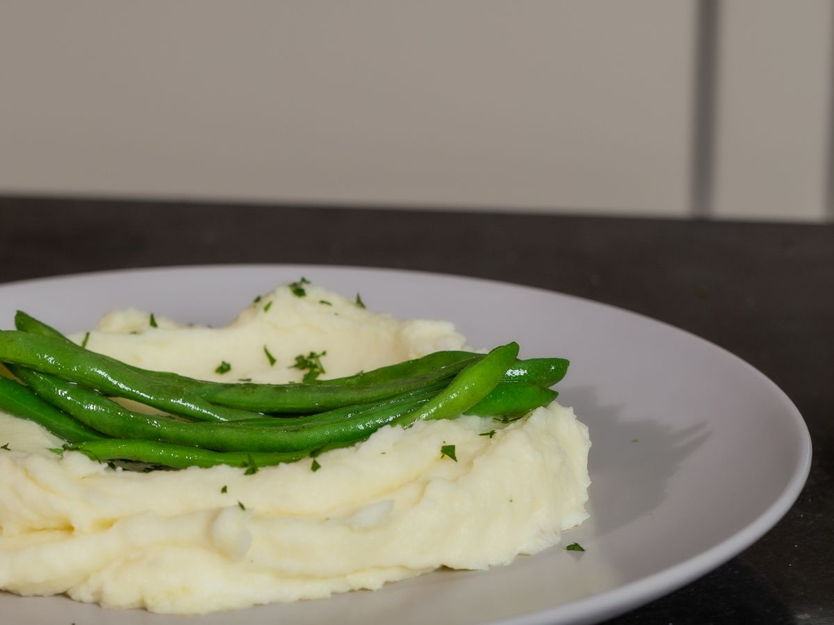 Mashed potatoes with green beans and parsley on a white plate
