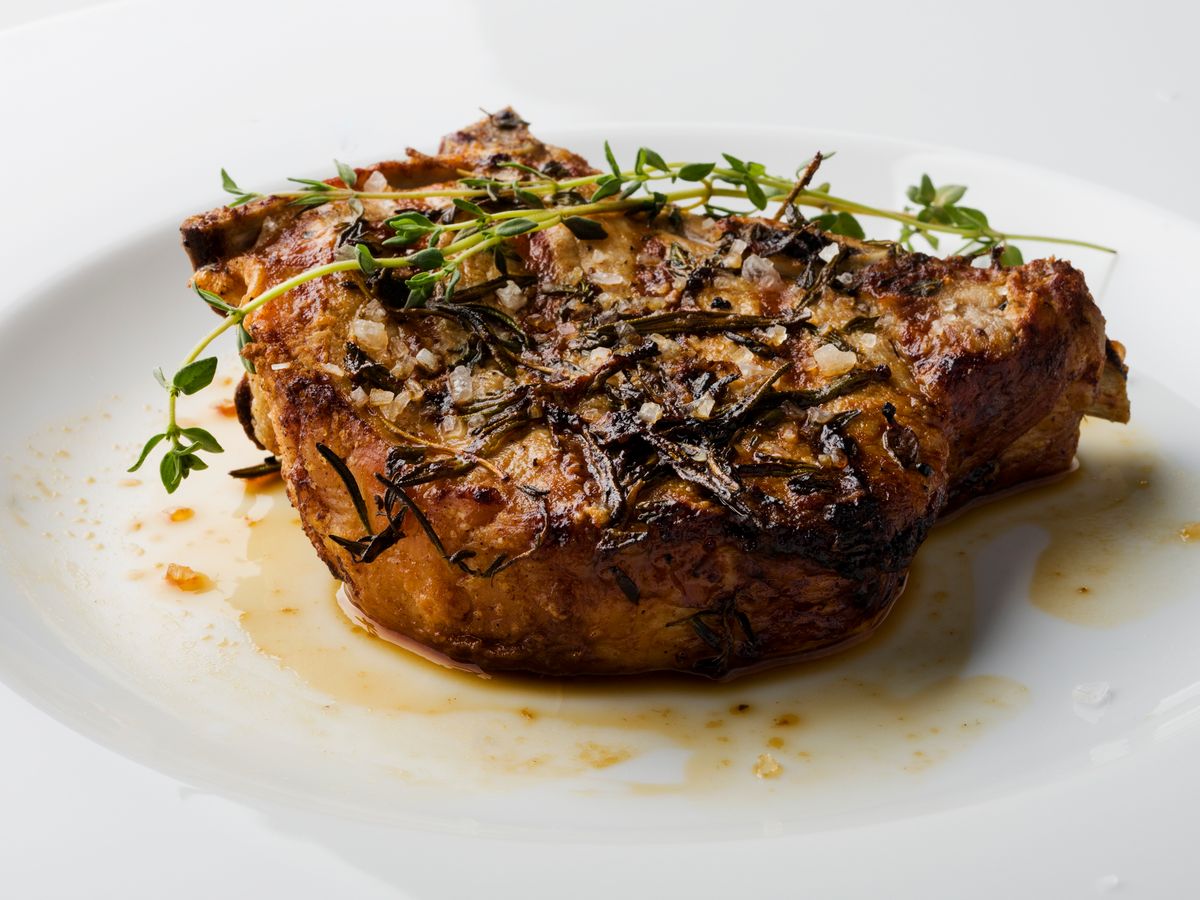 Herb-crusted pork chop with thyme on a white plate