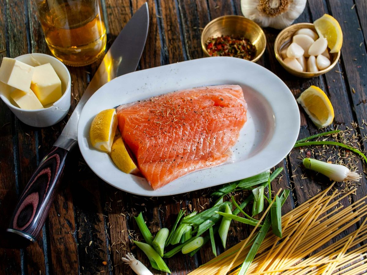 Raw salmon fillet with lemon wedges, garlic and spring onion