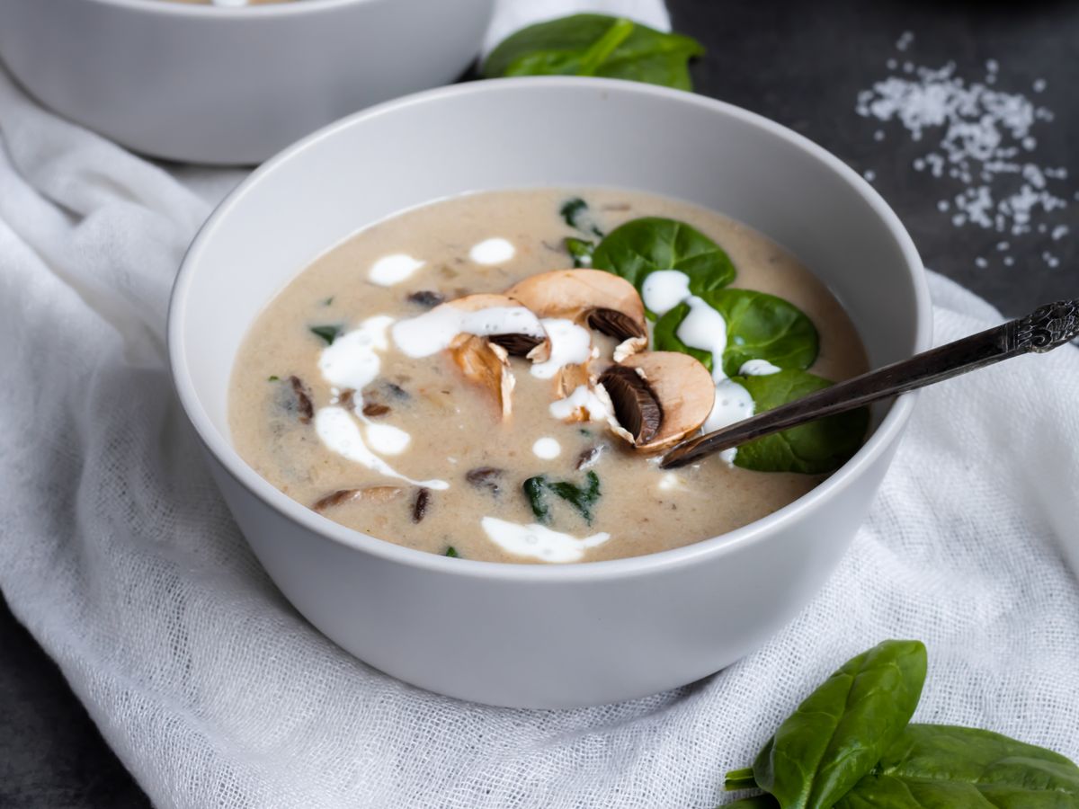 Cream of mushroom soup with sliced mushrooms and spinach leaves in a white bowl