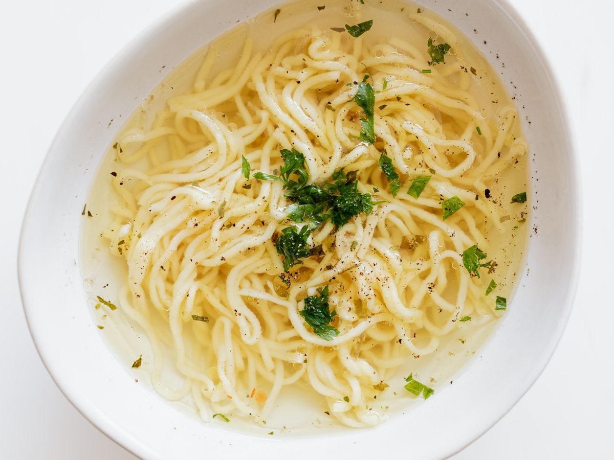 Noodles in clear broth with parsley and pepper in a white bowl, seen from above