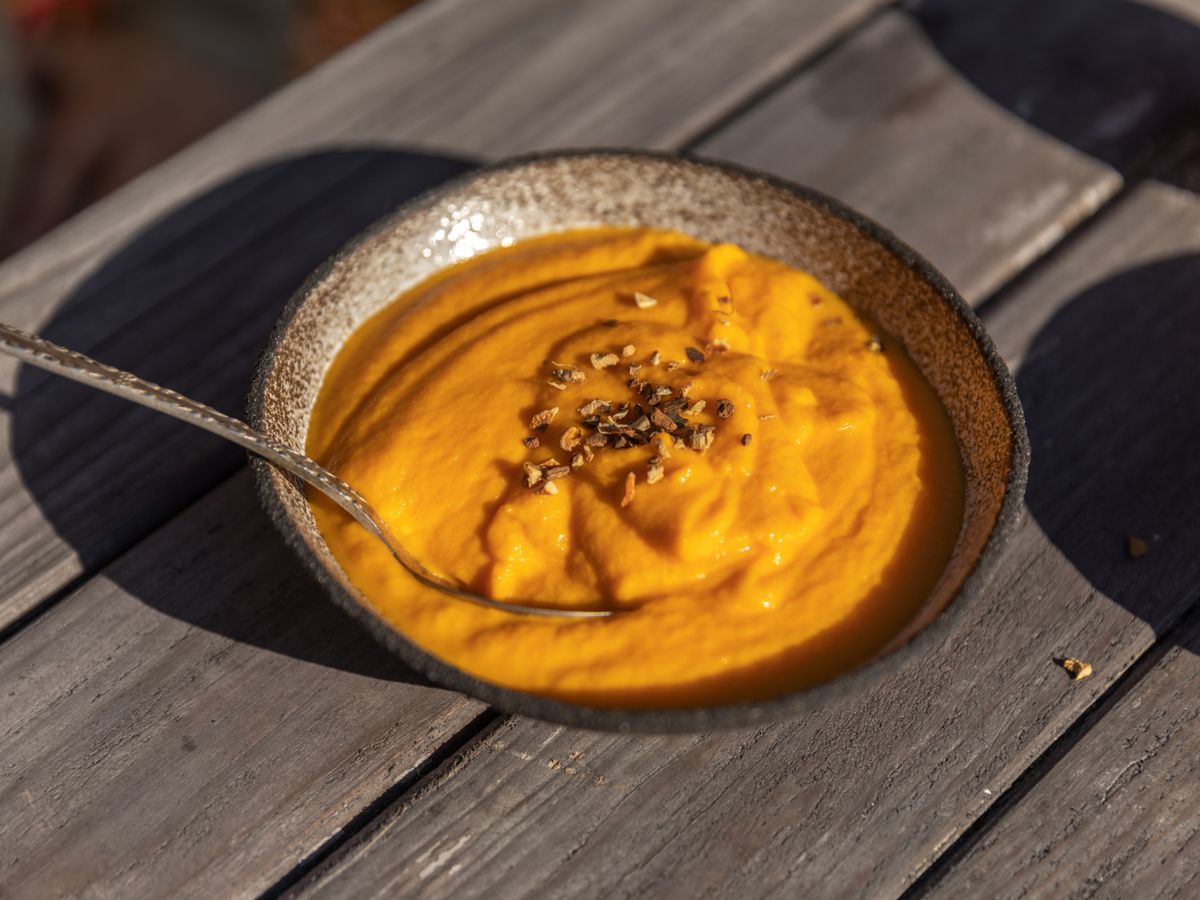 A bowl of smooth pumpkin soup with toasted seeds on a weathered wooden table