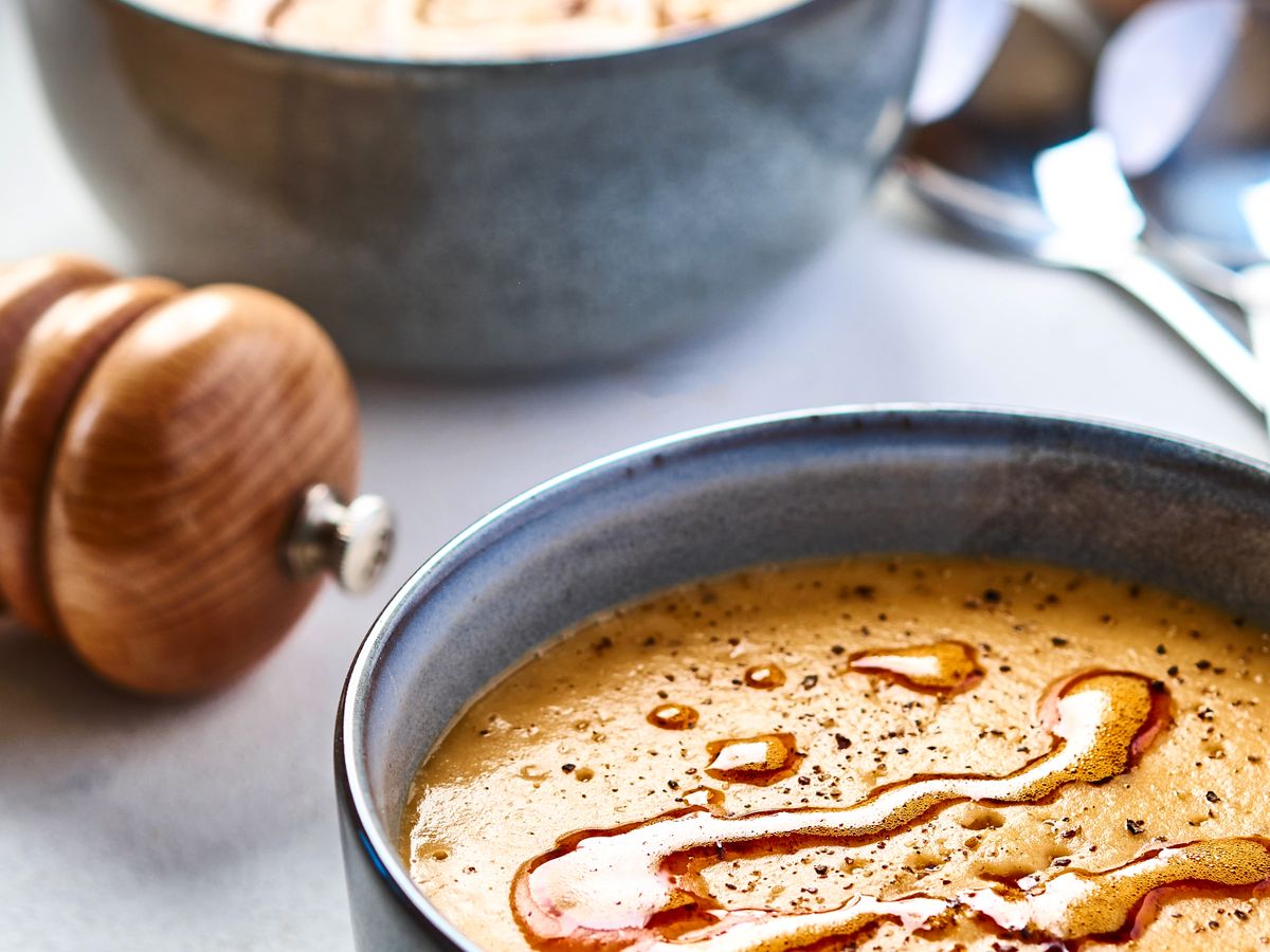 Red lentil soup in a grey ceramic bowl, drizzled with chilli oil, pepper mill beside it
