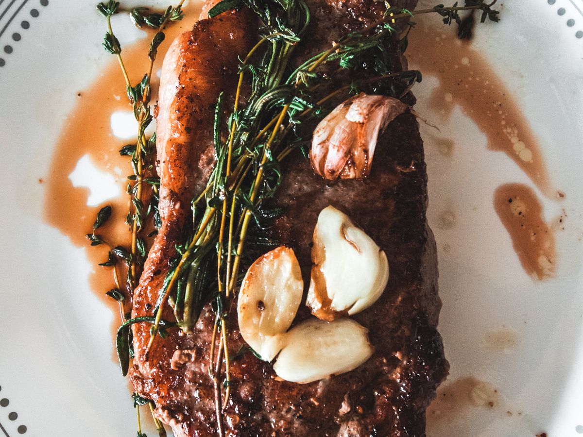 Sliced grilled steak with garlic and herbs on a white plate