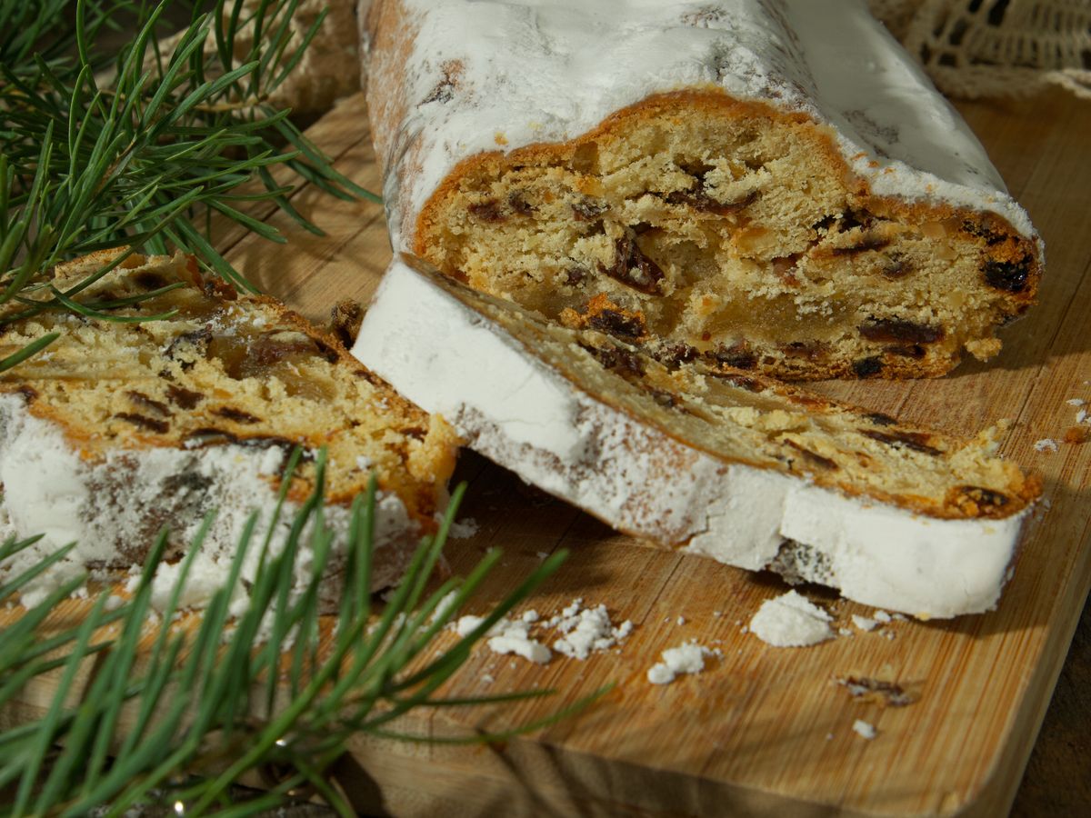 A sliced stollen dusted with icing sugar on a wooden board, raisins visible in the crumb